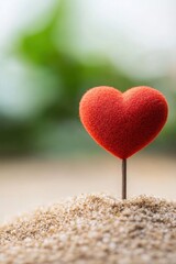 Fototapeta premium Vibrant red heart decoration resting on sandy surface, symbolizing love and warmth in a serene, blurred background.