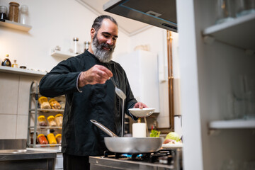 Professional chef is preparing meal in restaurant's kitchen. He makes a vegetarian lunch. He is adding food topping.