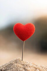 Fototapeta premium A vibrant red heart on a stick stands alone in the sand, symbolizing love and affection in nature.