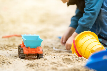 Little cute toddler boy 3.5 years old plays in the sandbox on a sunny spring day. Outdoor creative activities for kids. Toy truck and bucket. Focus on the car