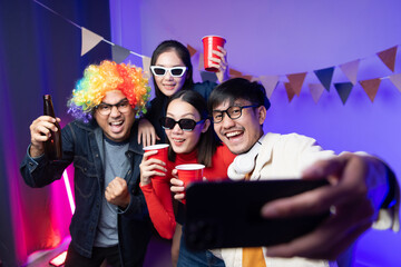 Group of Asian male and female friends Having fun dancing at a house party Take a selfie with a group of friends using your smartphone. A room lit up with disco neon lights. New Year's Eve party idea