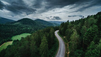 Aerial View of a Winding Mountain Road Surrounded by Lush Dark Green Forests, Showcasing Natures Beauty and the Serpentine Pathway Through the Scenic Landscape