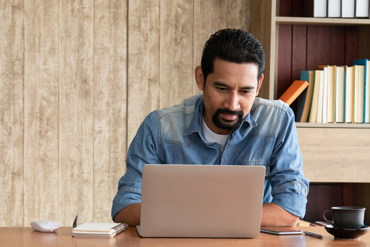 Portrait of happy mature business man in casual lifestyle with stylish short beard at workplace using laptop and smartphone