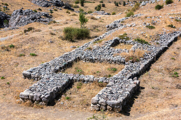 Hattusa archaeological site. Stone foundations of ancient structures, surrounded by dry grass and...