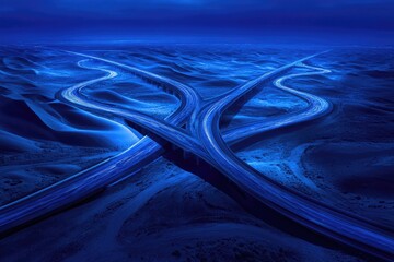 Night aerial view of a complex highway interchange crossing sand dunes, illuminated by vehicle light trails.