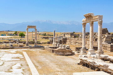 Fototapeta premium Ancient temple courtyard in Laodicea featuring marble columns, stone ruins, and a scenic mountain backdrop under a blue sky. Denizli, Turkey (Turliye)