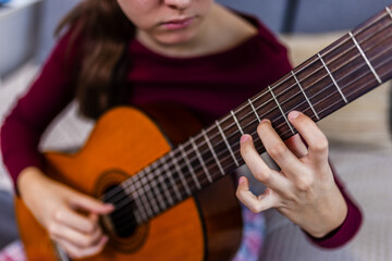 Young woman strumming her guitar in the comfort of her room.