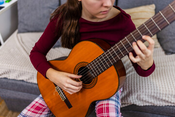 Young woman strumming her guitar in the comfort of her room.