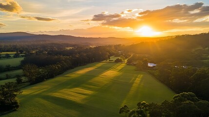 Obraz premium Aerial view of a stunning sunset over a rural landscape with golden hour light illuminating the green fields and forests.