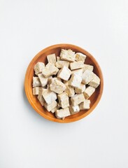 Uncooked tempeh pieces in a wooden bowl on a white background. Top of view. 