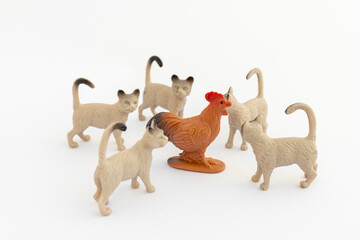 Miniature cats surrounded and trying to hunt a plastic toy rooster.