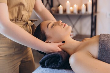 Masseuse giving relaxing neck massage to young woman in spa