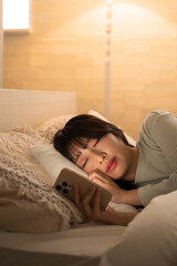 スマホを見ながら寝落ちしてしまった女性　黄色い間接照明