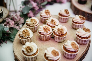 Delicious walnut-topped cupcakes on a rustic wooden platter surrounded by flowers.