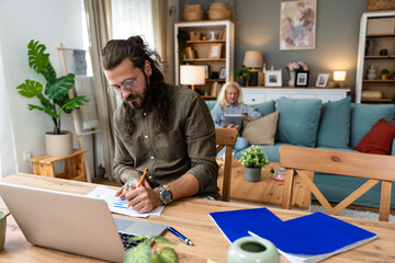 Confident couple office workers work at home, young caucasian couple sit at table using laptop...