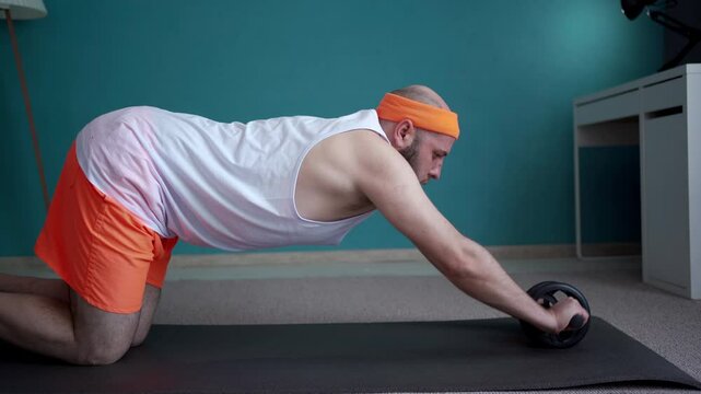 Middle aged man in orange headband exercising with ab wheel on floor at home