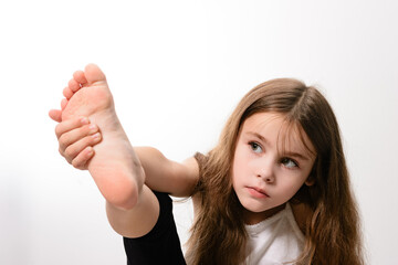 A young girl with long brown hair is captured in a moment of stretching, her focus evident. She...