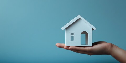 Naklejka premium Hand holding a miniature house model against a blue background