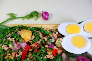Spicy vegetable salad with minced pork and halved boiled eggs on a light colored wooden plate. Next are red onions and vegetables.

ไอคอนยืนยันโดยชุมชน