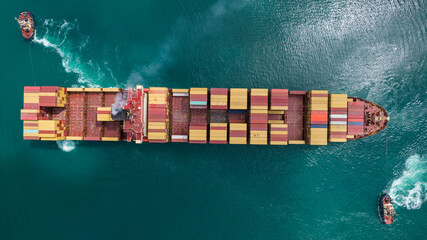 Aerial top view of tugboats maneuvering container cargo ship. Container cargo ship in harbor...