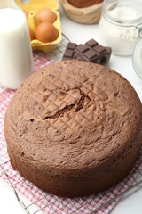 Tasty chocolate sponge cake and ingredients on white wooden table, closeup