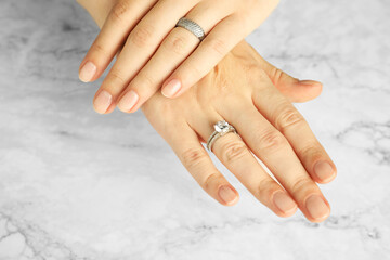 Beautiful bijouterie. Woman wearing different stylish rings at white marble table, closeup