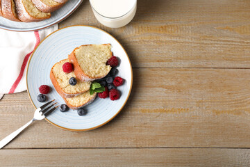 Pieces of freshly baked sponge cake, berries and milk on wooden table, top view. Space for text