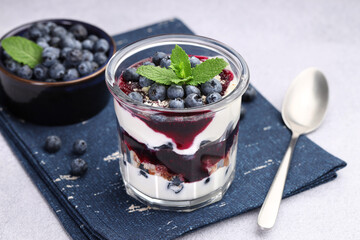 Tasty trifle dessert. Blueberries, sponge cake and whipped cream in glass on light grey table