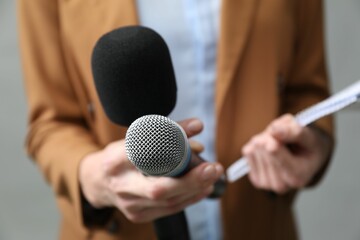 Journalist with microphones and notebook on grey background, closeup
