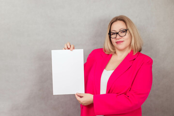 Naklejka premium Portrait of a charming blonde plus size in glasses for vision, in her hands a white sheet of paper with space for text. Copy space
