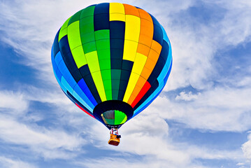 Colorful hot air balloon flying over blue sky with white clouds	