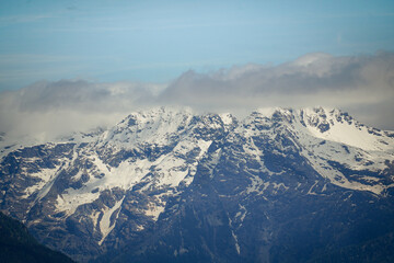 Fototapeta premium Snow covered rocky mountain peaks with low clouds, Switzerland
