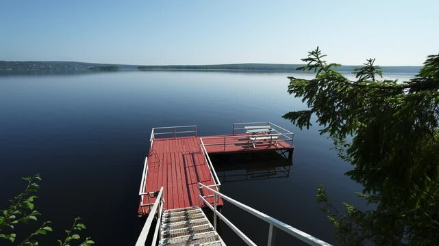 The tranquil lake dock is beautifully surrounded by lush greenery in a serene location. Clip
