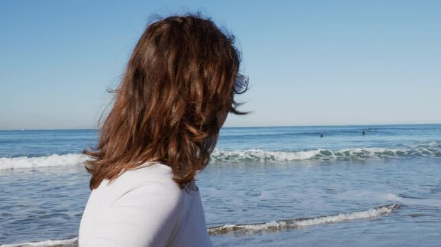 Mujer disfrutando al caminar por la orilla de la playa, mira hacia el mar, surfista de fondo plano corto