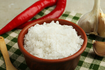 Sea salt in bowl, garlic and chili peppers on table, closeup