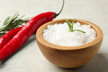 Sea salt in bowl, rosemary and chili peppers on grey table, closeup