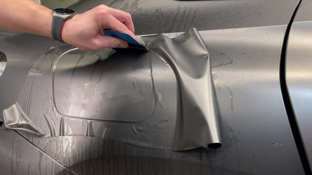 A specialist in wrapping a car with gray matte vinyl or ppf film in the process of work. Car wrapping specialists cover the car with gray matte vinyl film. Gray matte vinyl foil. Selective focus.	