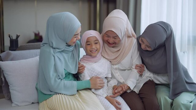 Cheerful muslim family, including women and a young girl wearing hijabs, sharing love and laughter while sitting together, symbolizing unity, joy, and family bonds at home.
