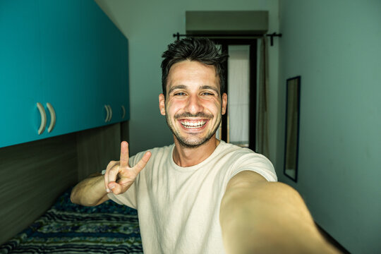 Happy handsome guy taking selfie with smartphone at home - Laughing guy looking at camera - People and technology concept