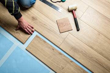 Worker installing laminate flooring in apartment under renovation.