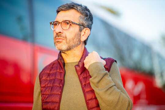 Thoughtful man standing near a red bus outdoors - Powered by Adobe