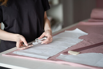 A designer carefully marks fabric with chalk for pattern cutting; seamstress holds scissors over...
