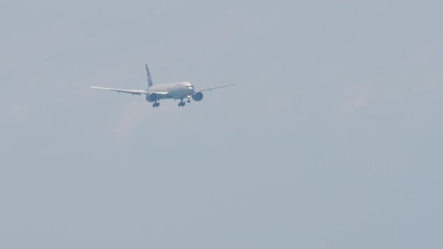 Airliner approaching landing, side view. Jet plane with unrecognizable livery descending, arriving, long shot. Aircraft in the blue sky