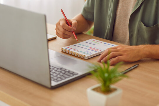 Cropped photo of businessman writing tasks and to do list in his notepad sitting at the desk with laptop at home or at office. Man looking to schedule calendar planning daily appointment. - Powered by Adobe