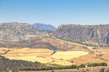 The mountainous land of Andalusia near Ronda town in Spain. Serene landscape of rolling hills, dry fields, and rugged mountains under a clear blue sky. A peaceful, sun-drenched vista.