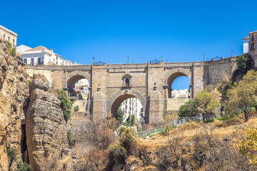 The Puente Nuevo bridge in El Tajo gorge in Ronda town in Spain. Ancient stone bridge spanning a deep gorge, with buildings visible on either side under a clear blue sky.
