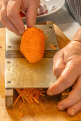 Chef grates carrots on an old homemade metal grater. Close-up