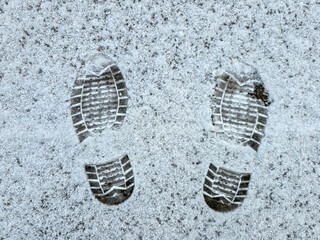 two detailed boot prints in freshly fallen snow, showcasing the textured tread patterns. The simplicity of the white snow contrasts with the defined marks, evoking a sense of winter and exploration