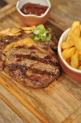A plate of steak and french fries sits on a wooden cutting board. The steak is cooked medium rare and is accompanied by a side of fries. The dish is presented in a casual and inviting manner