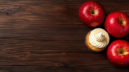 Three red apples and a cupcake on a wooden table